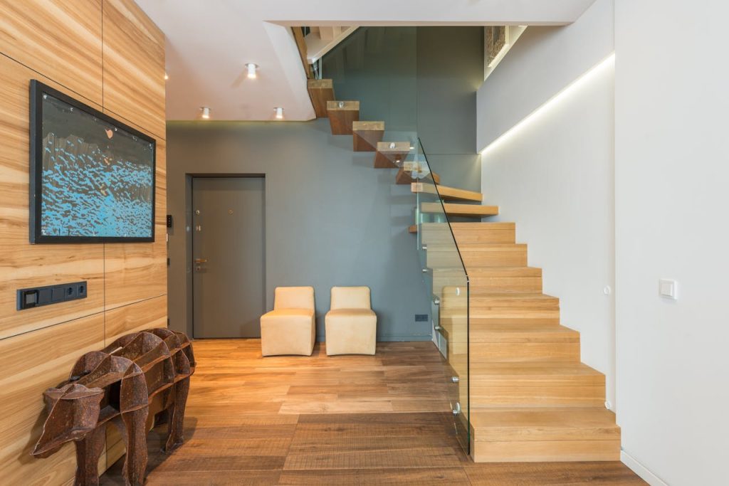 pexels-photo-7018824 Contemporary stylish house hallway interior with creative statue under TV set cozy chairs and wooden stairway